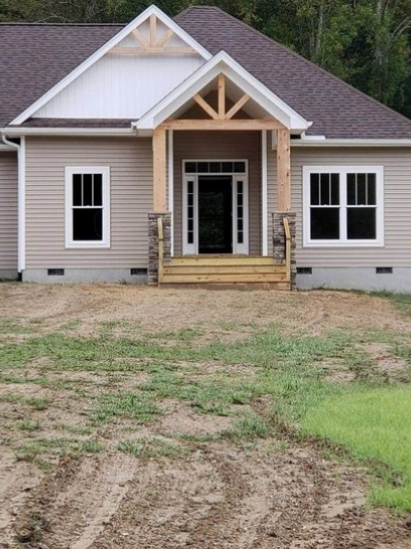 Two-story home with light siding, covered front porch, white door with glass panes, dirt yard and driveway, black-framed windows, no landscaping.
