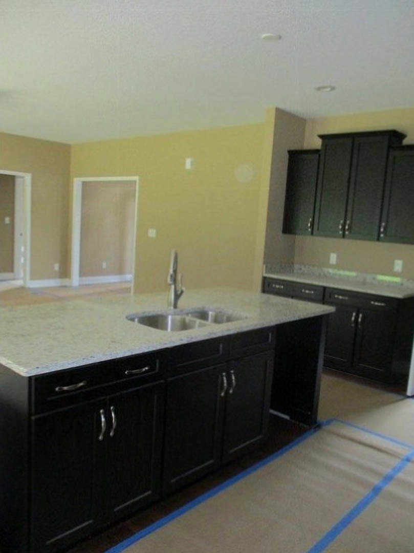 Black kitchen cabinets with granite countertops, stainless steel sink and faucet, tile backsplash, blue painter’s tape on the counter, light-colored floor tiles