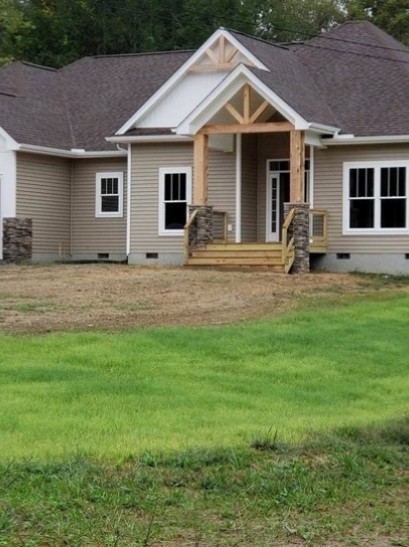 Two-story home with white-framed windows, covered front porch, wooden fence displaying a flag, and manicured green lawn