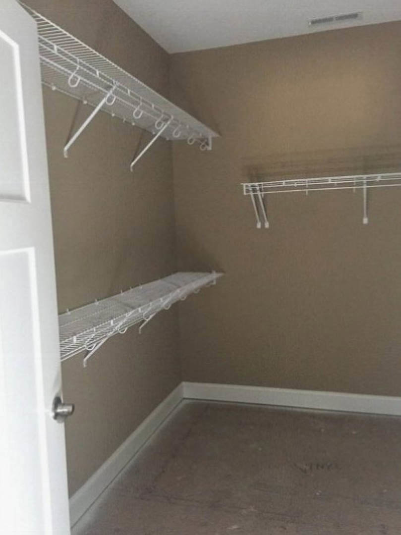Walk-in closet with white built-in shelves, silver hooks, grey plank flooring, and a white paneled door with chrome handle