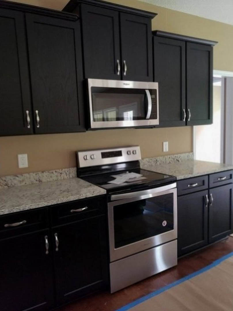Black kitchen cabinets and appliances including a built-in microwave above lower cabinets, white electrical outlet on backsplash, dark countertops, and modern finishes.