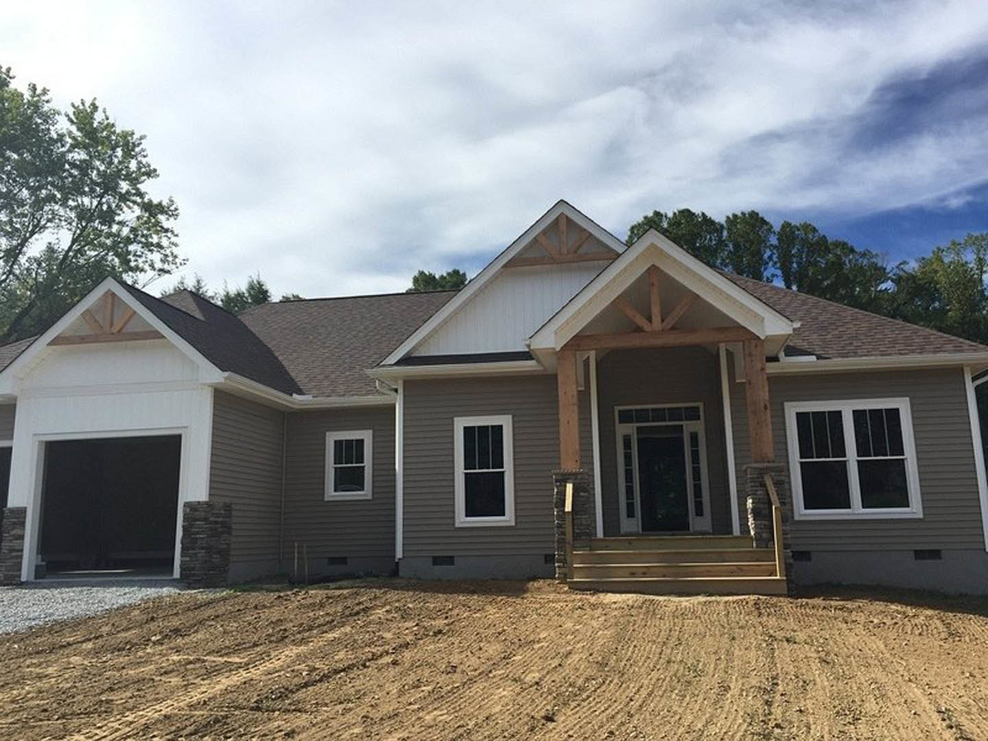 White single-story house with horizontal siding, white-trimmed windows, and a white front door with glass panel, set on a dirt yard under a cloudy sky