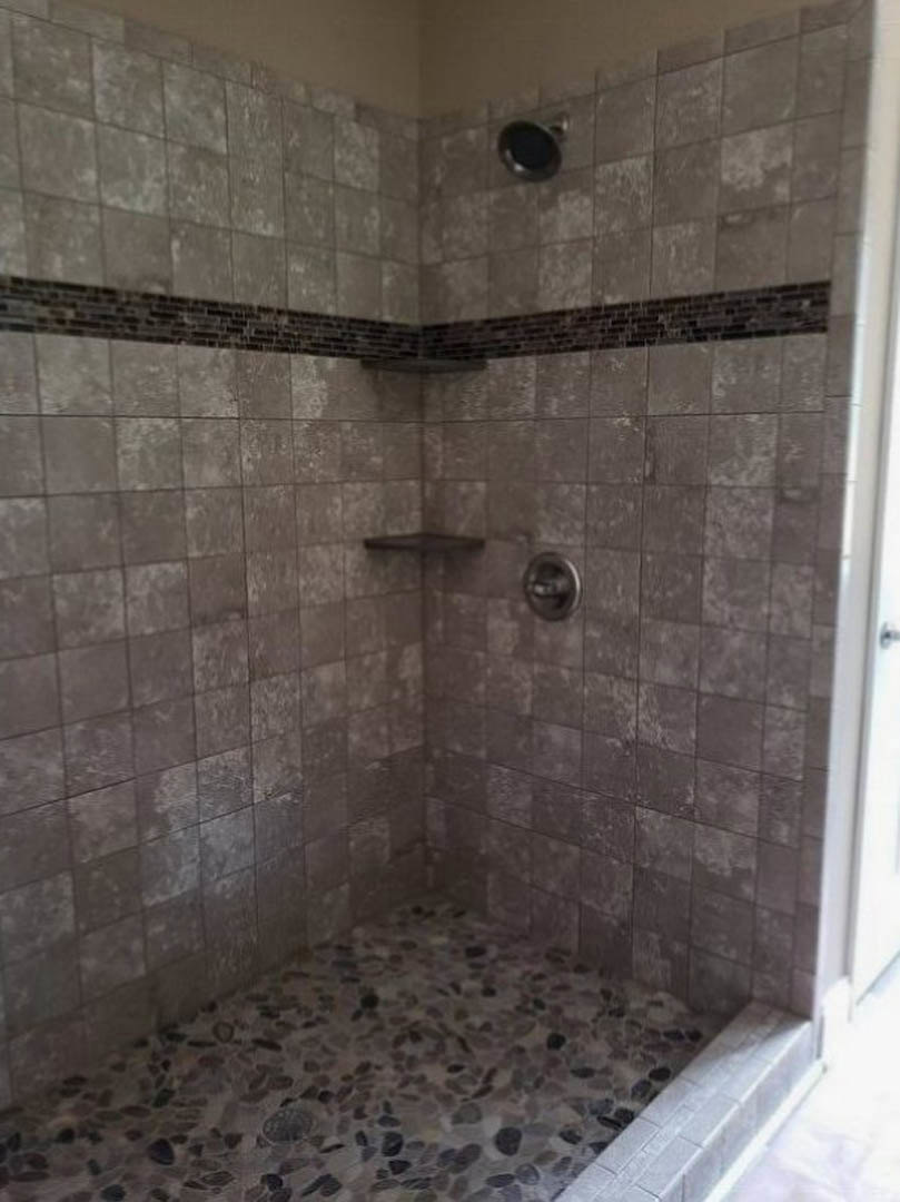 Walk-in shower with grey tile floor, marble tiled walls, and modern plumbing fixtures