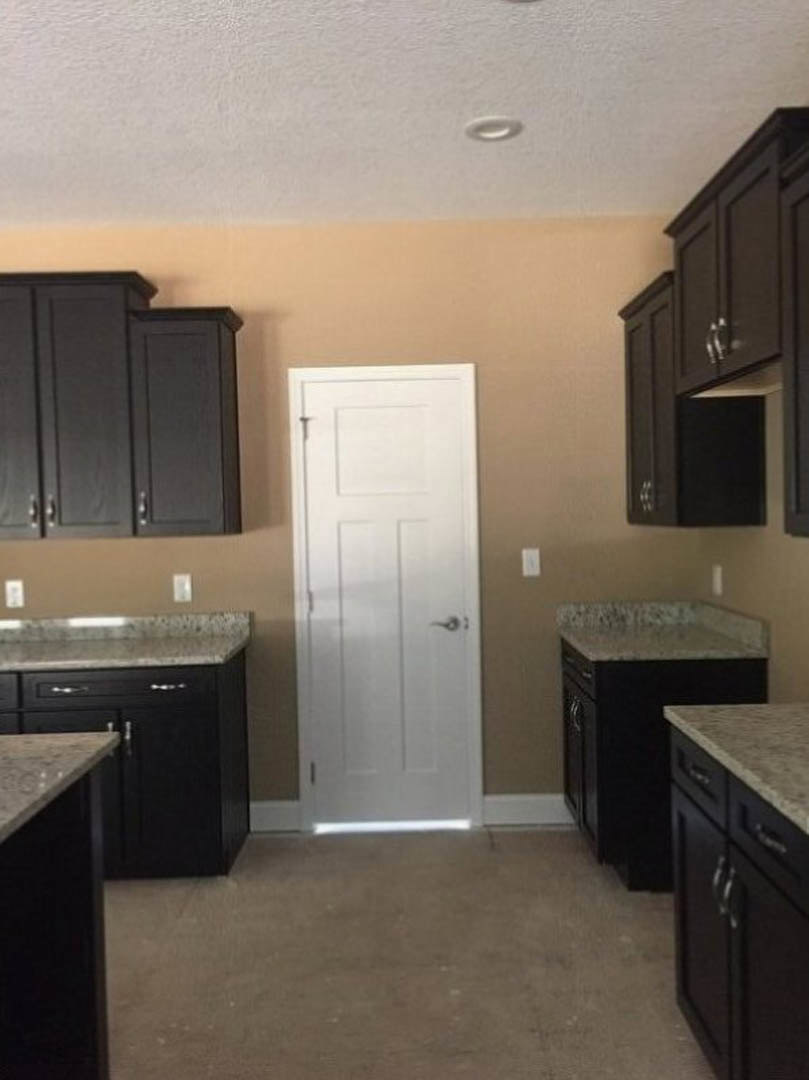 Black kitchen cabinets with brushed metal handles, white door with silver handle, light stone countertops, stainless steel sink, and wood flooring