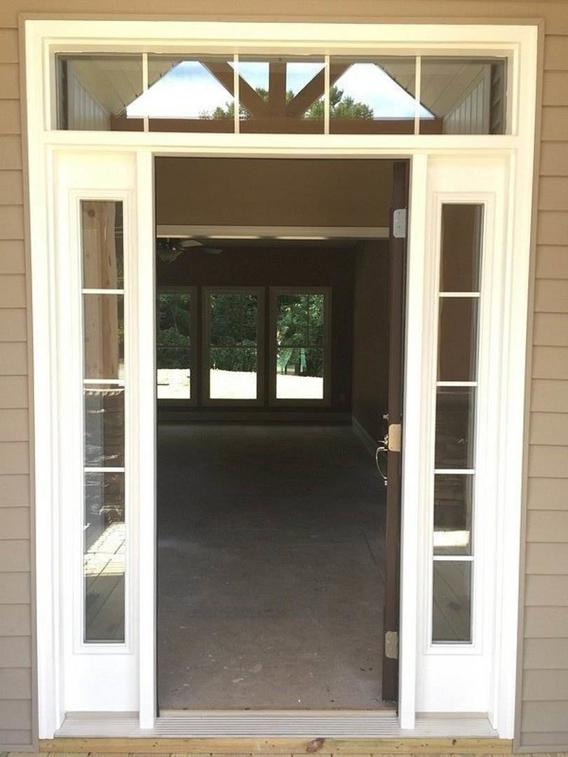 Modern front door with black frame, adjacent windows featuring wooden beams, exterior view includes landscaped trees in the background
