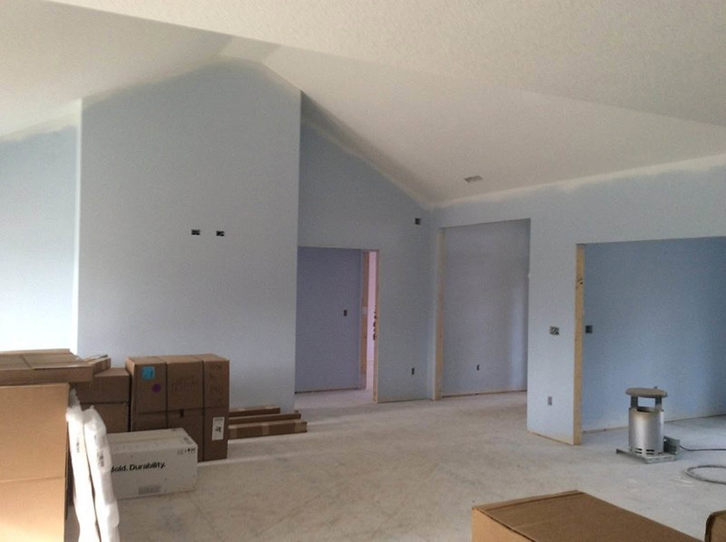 White-painted wall with stacked cardboard boxes, metal trash can, and small wooden stool on light flooring