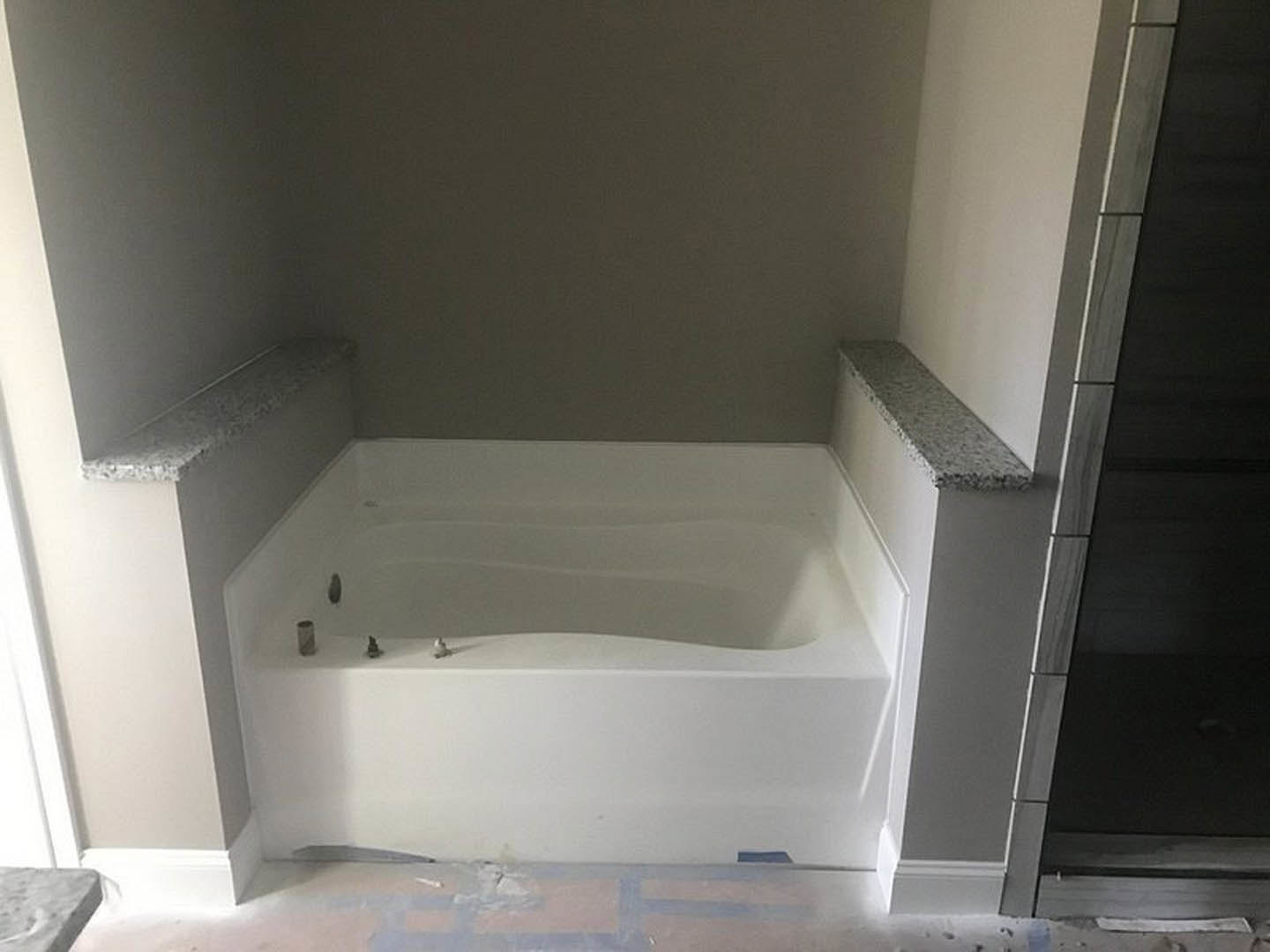 Freestanding white bathtub with chrome faucets beside tiled wall and plaster finish in modern bathroom