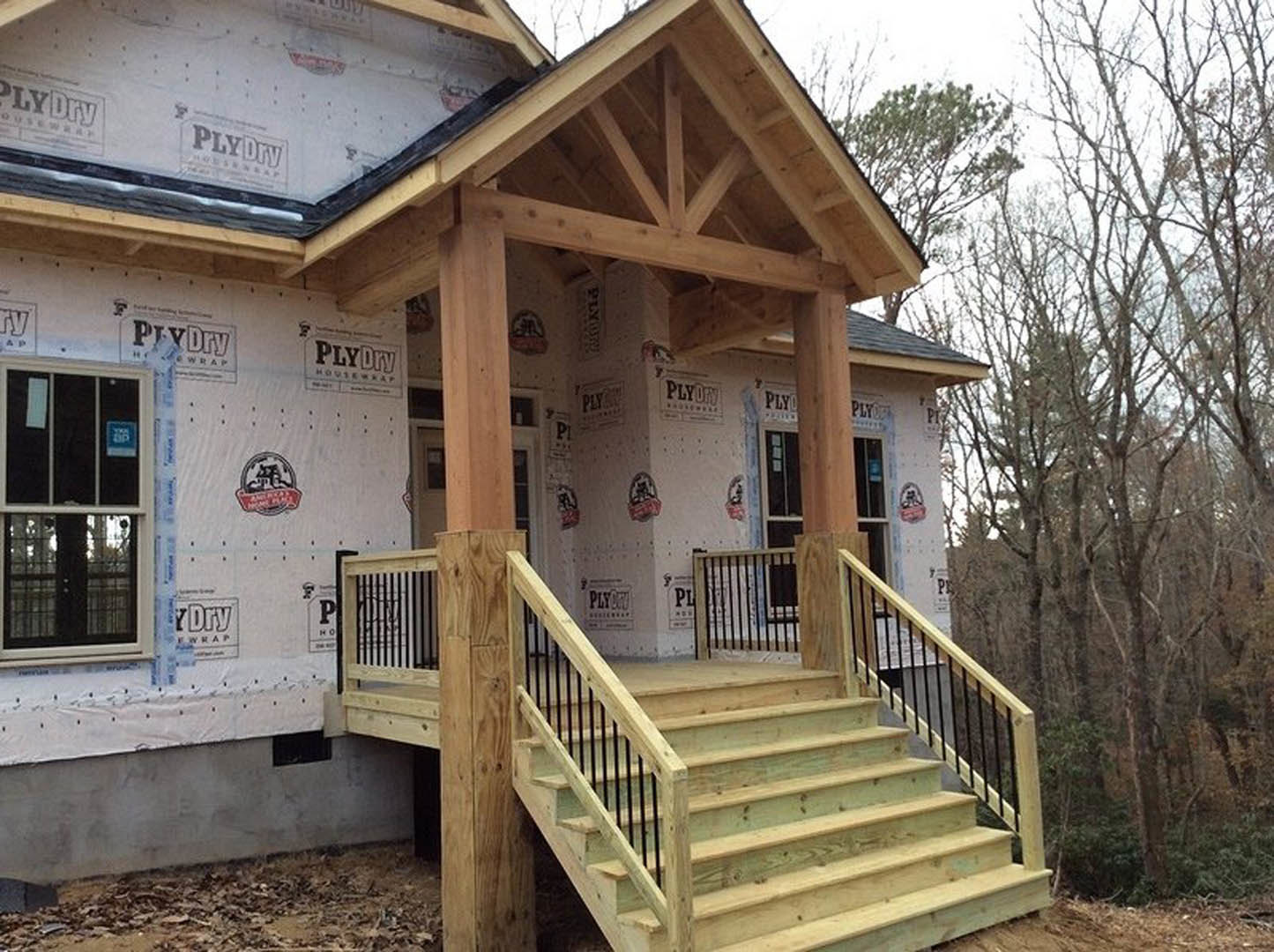 Wooden exterior stairs leading to unfinished porch, exposed lumber framing, window installed, white siding partially visible, construction materials scattered around, tree in