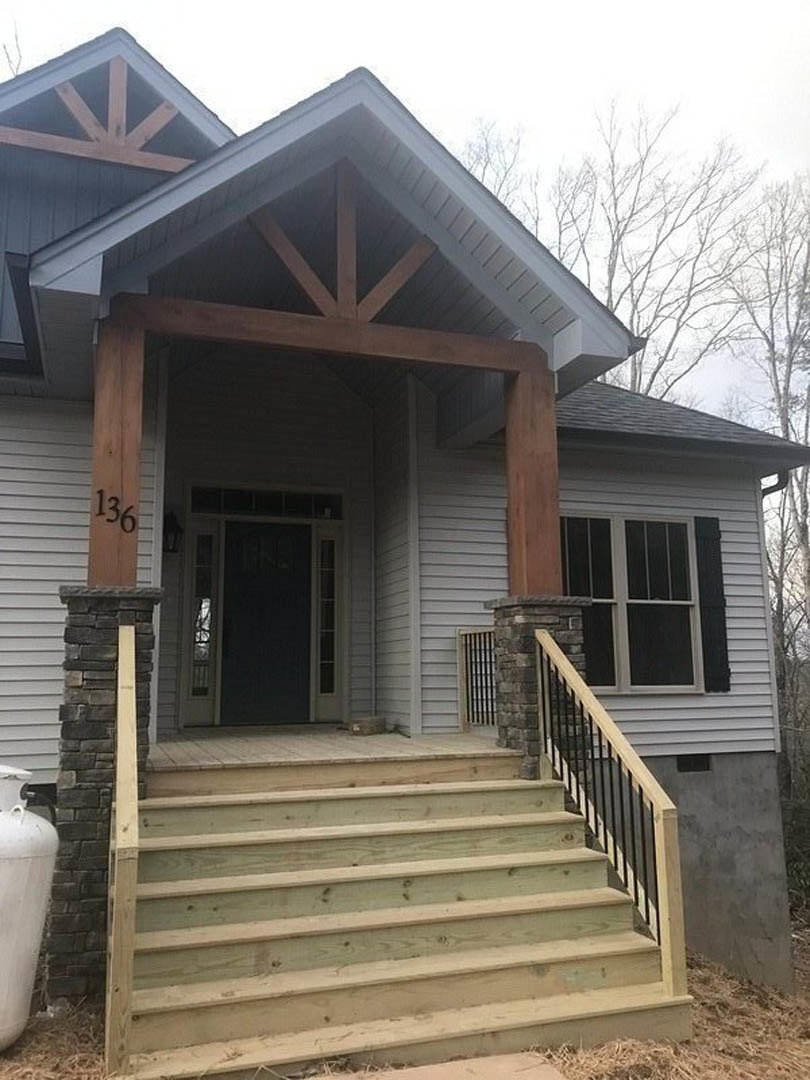 White siding house with black trim, wood porch and stairs, dark front door with glass panel, large window, blue sky overhead