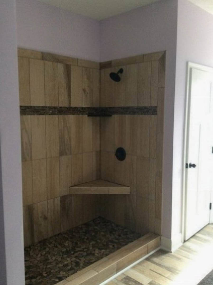 Walk-in shower with light gray tile walls, built-in wood shelf, and plaster finish