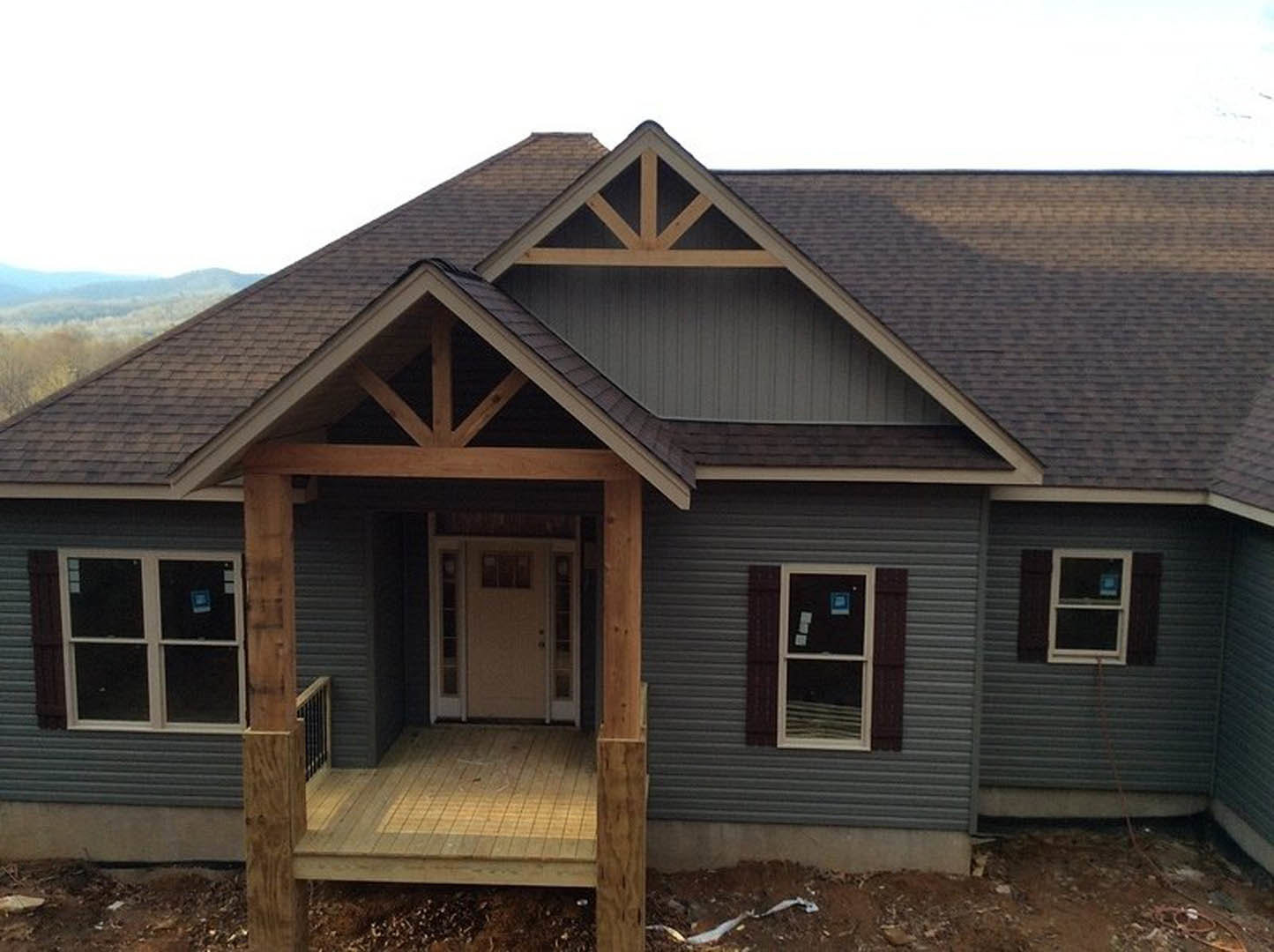 Partially built house with exposed wooden porch deck, white framed window, white door with glass insert, gray siding, and shingled roof