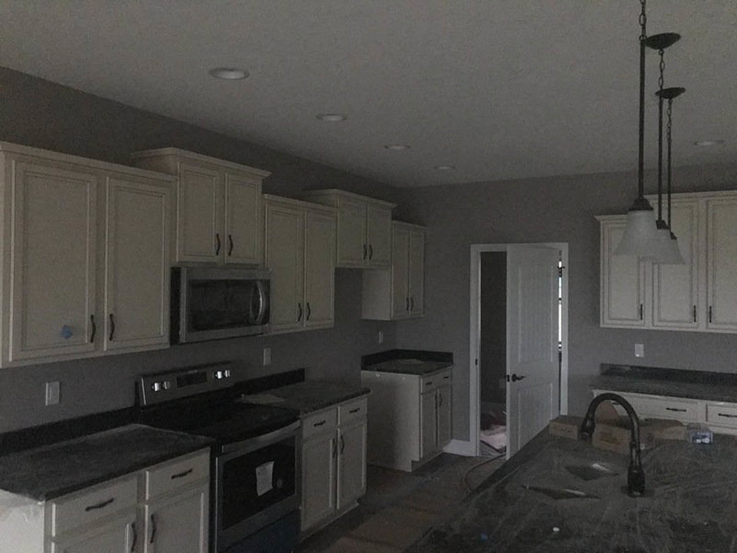 White shaker cabinets with black stone countertop, stainless steel microwave and stove, black faucet over undermount sink, light walls, modern kitchen appliances