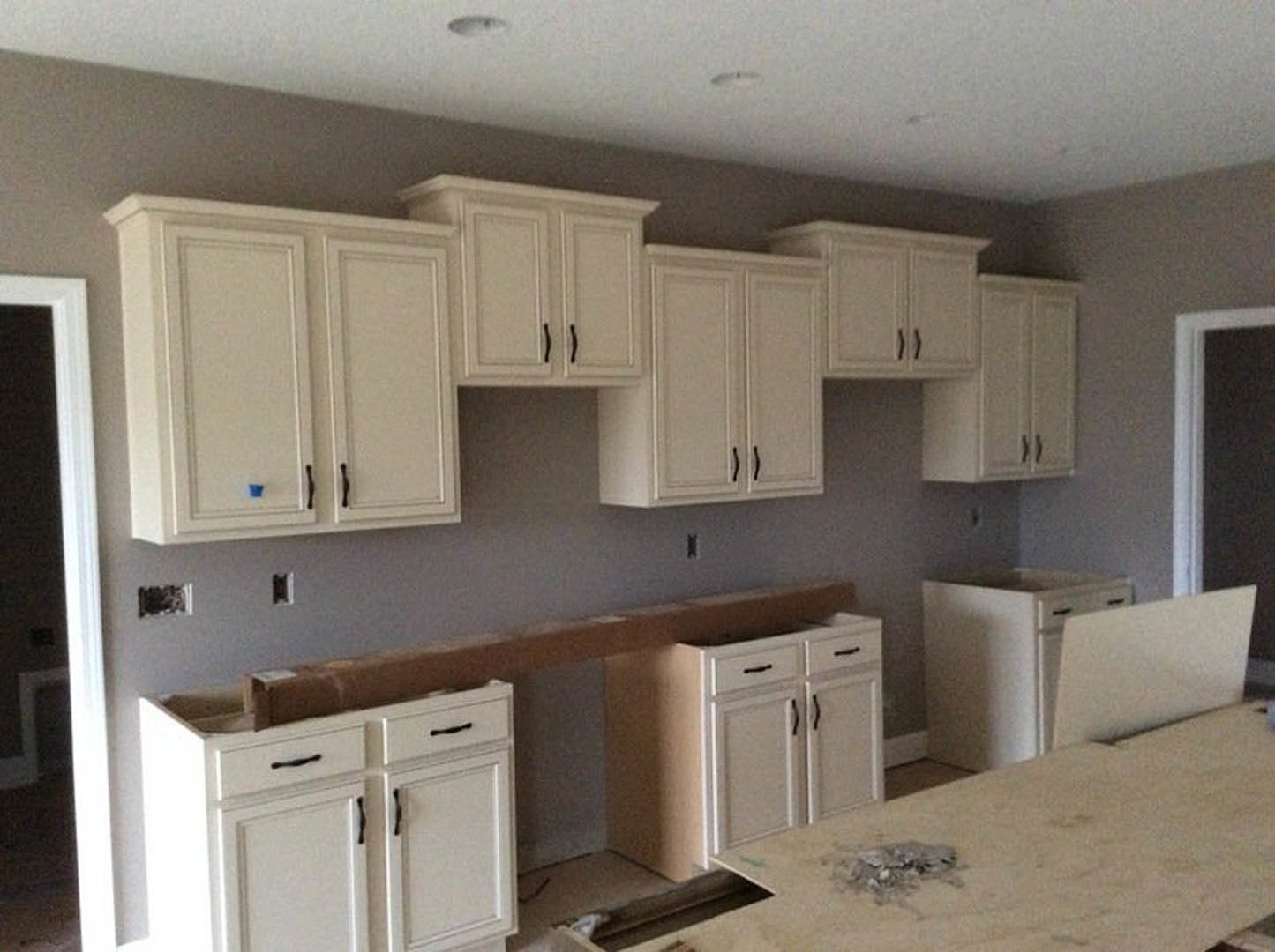 White kitchen cabinets with black handles, light stone countertops, stainless steel sink, wooden dining table, and a laptop on the counter.