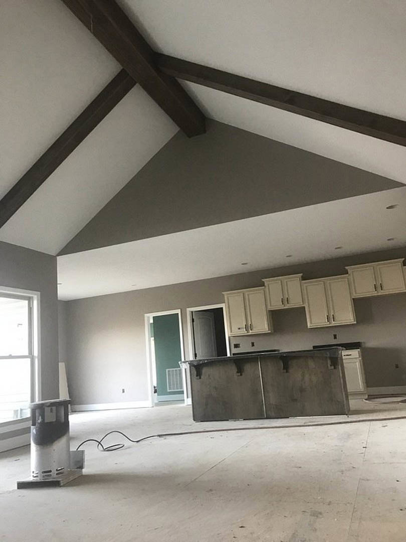 Modern kitchen with white shaker cabinets, quartz countertops, stainless steel appliances, large window for natural light, and open white door leading to adjacent room