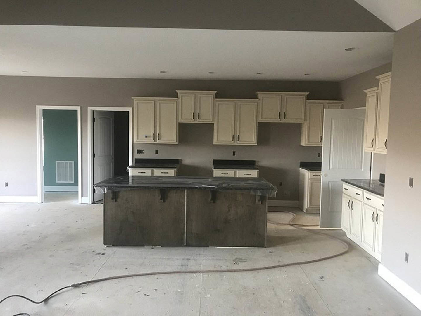 Marble island with waterfall edge, white shaker cabinets, stainless steel sink, green accent wall, hardwood flooring, recessed lighting