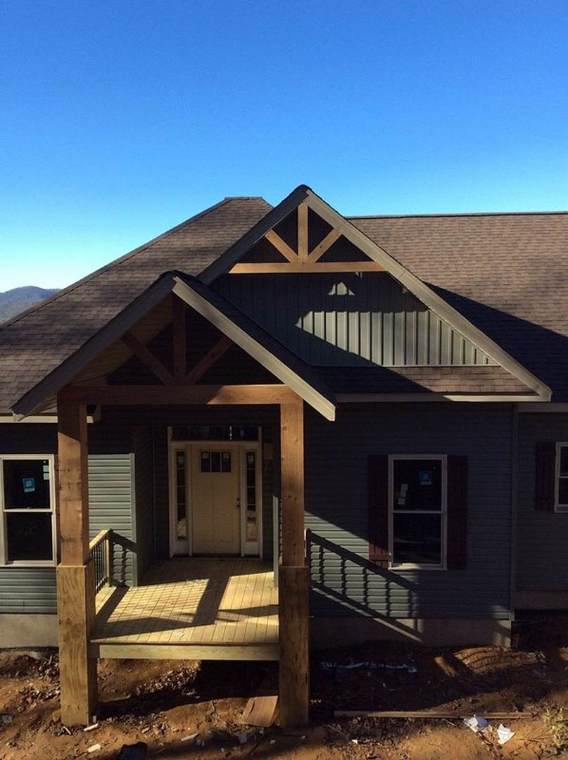Gray siding house with covered front porch, white trim, glass-paneled white door, large windows, shingled roof, and landscaped entry.