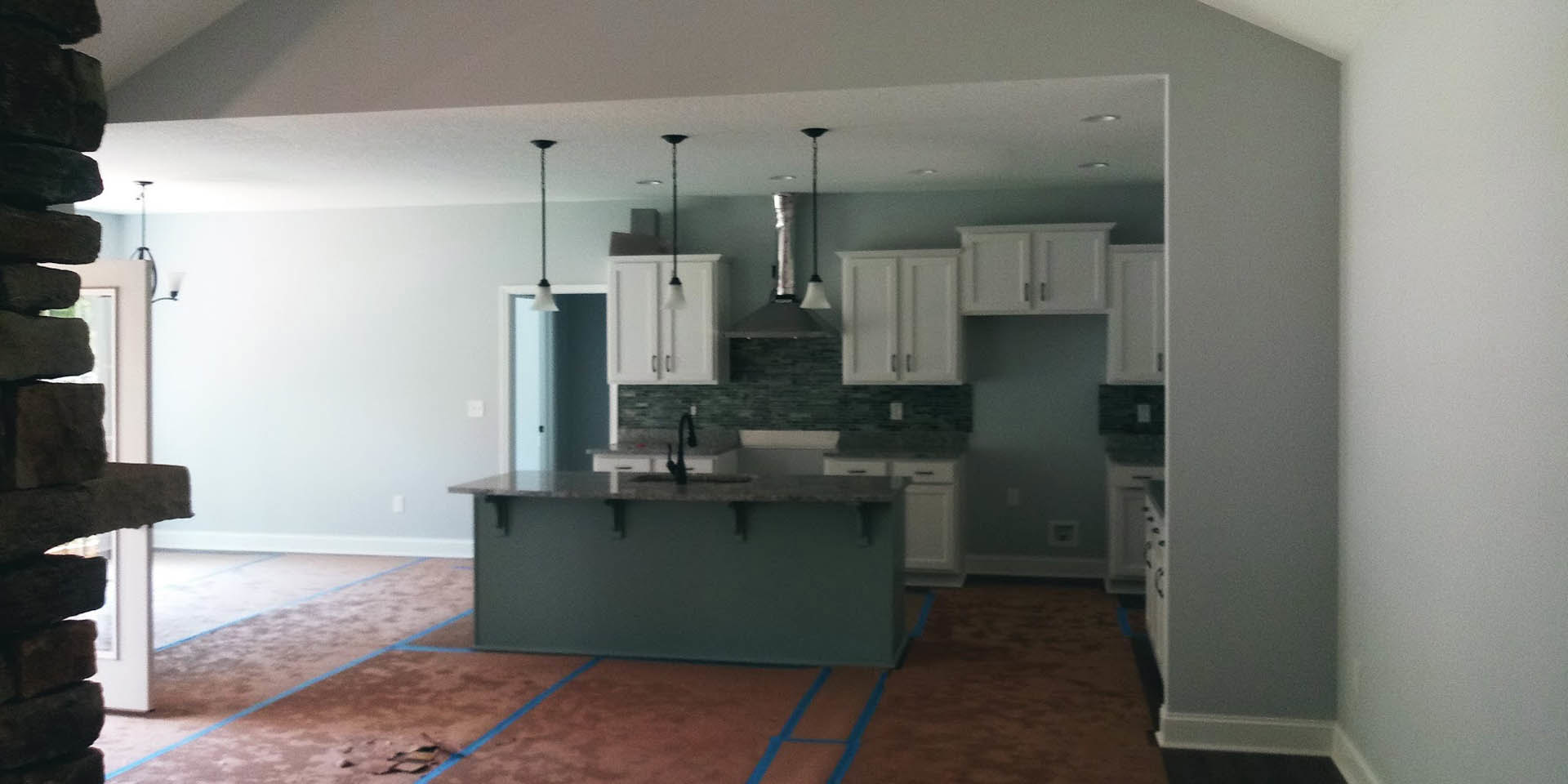 Open kitchen with white cabinets, central island featuring built-in sink, brown tile flooring with blue accent line, recessed lighting under upper cabinets, electrical outlet on