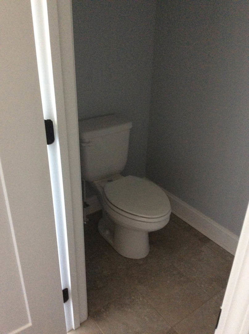 White toilet with closed lid in a compact bathroom, surrounded by light-colored tile walls and floor.