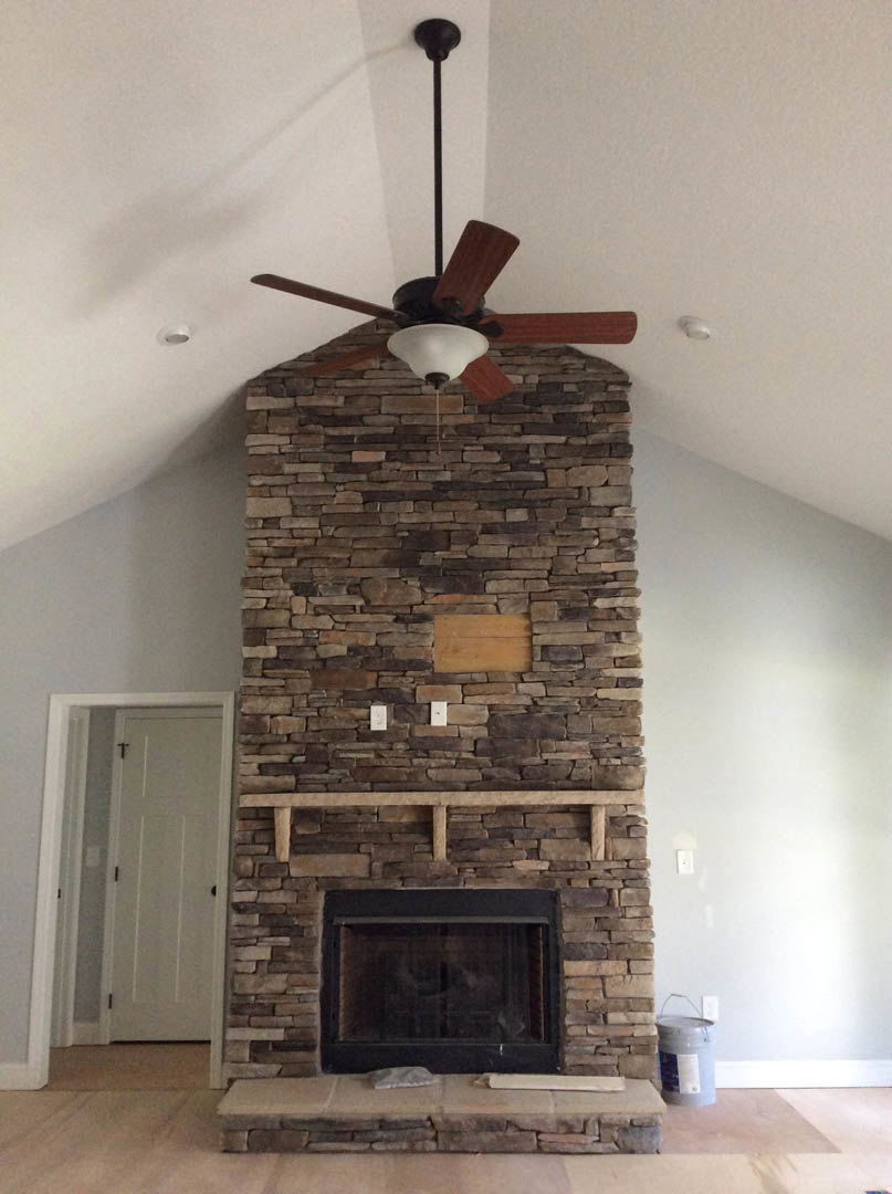 Stone fireplace with built-in shelf, ceiling fan installed inside firebox, white door with black knobs, window set in fireplace, close-up of metal bucket and brick wall, hardwood