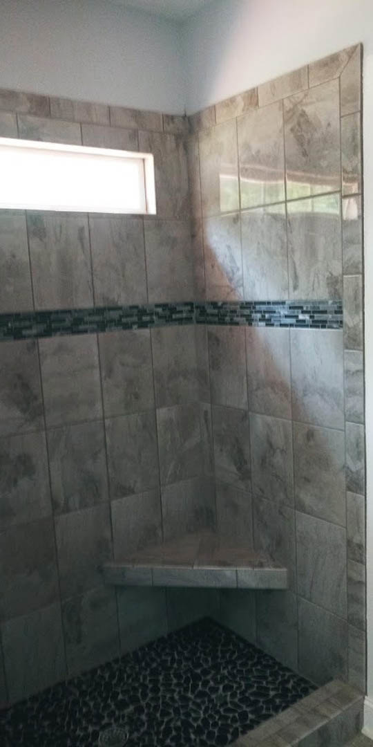 Shower with marble tile wall, black and white tile floor, white rectangular ceiling light, window, and plaster walls