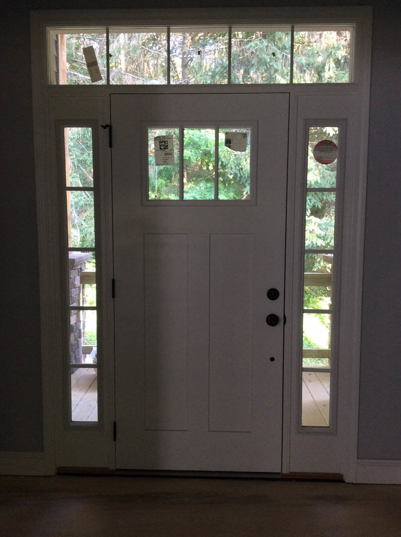 White paneled door with rectangular glass windows, silver door handle, and light wood flooring in a residential entryway