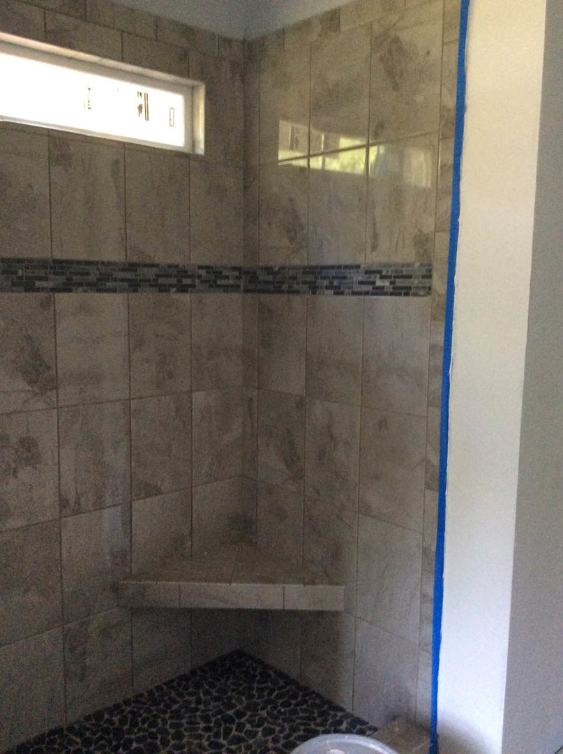 Corner shower with marble tile walls, glass enclosure, and stone floor in a modern bathroom