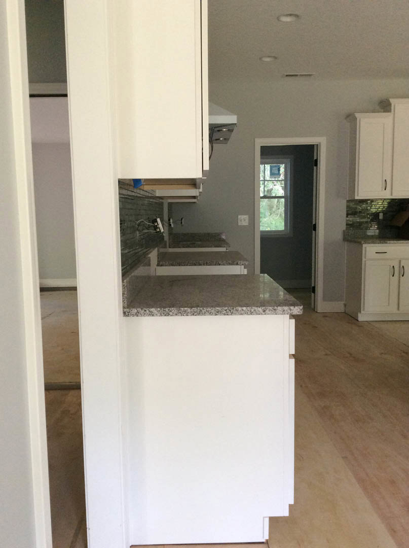 Kitchen with white shaker cabinets, black handles, granite countertops, stainless steel sink, window with black frame, light-colored walls, and hardwood flooring