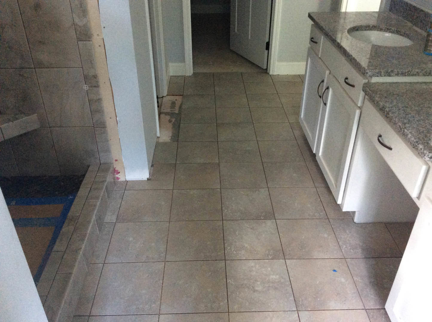 Bathroom with grey tile floor and black grout, white cabinets, undermount sink, glass-enclosed shower, and granite countertop
