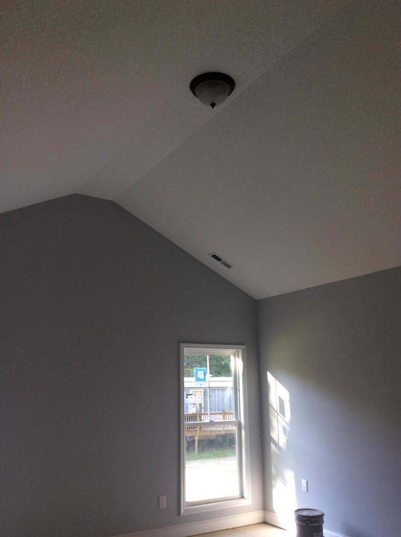 Bright room with white plaster walls, large window overlooking deck, modern ceiling light fixture, and visible trash can near the corner