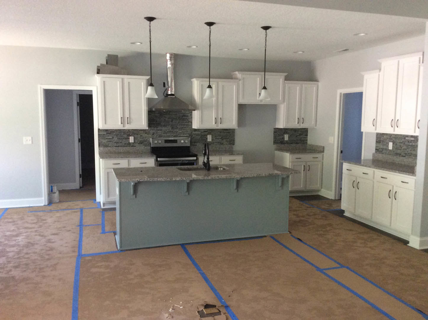 Modern kitchen featuring a central island with a built-in sink, stainless steel stove, white cabinetry, light countertops, and hardwood flooring.