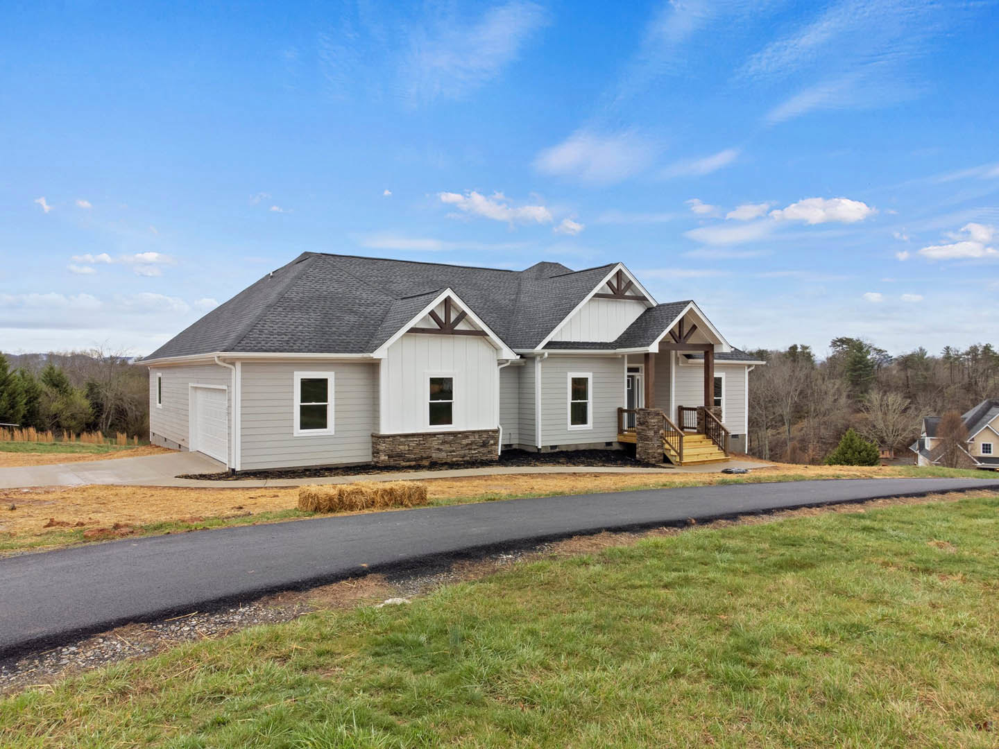 Two-story home with gray siding, white trim, shingled roof, concrete driveway, manicured lawn, and wooden steps leading to the front entrance