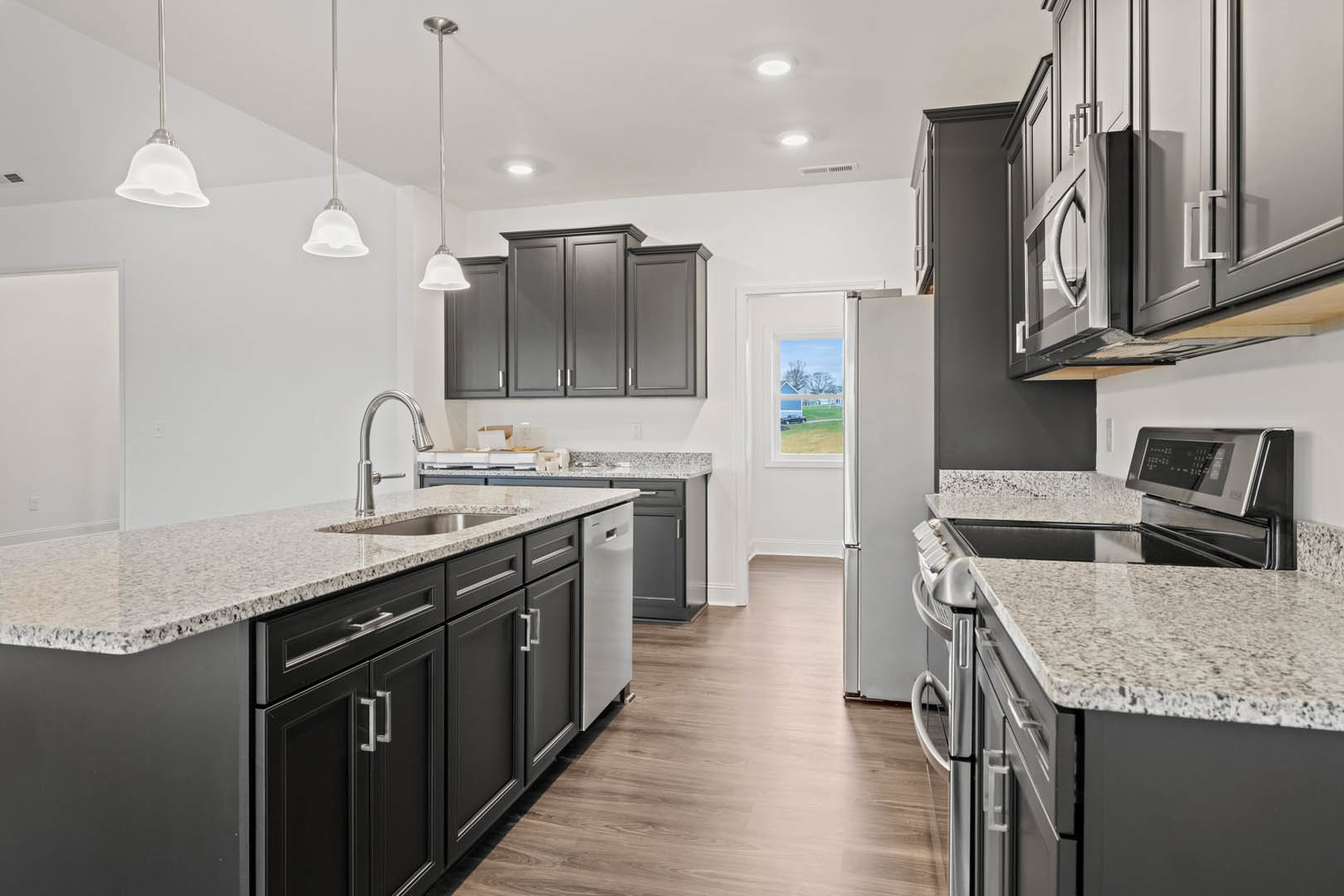 Black kitchen cabinets with granite countertops, stainless steel stove, modern light fixture, grey cabinetry, chrome faucet, and a black and white flag on a white pole