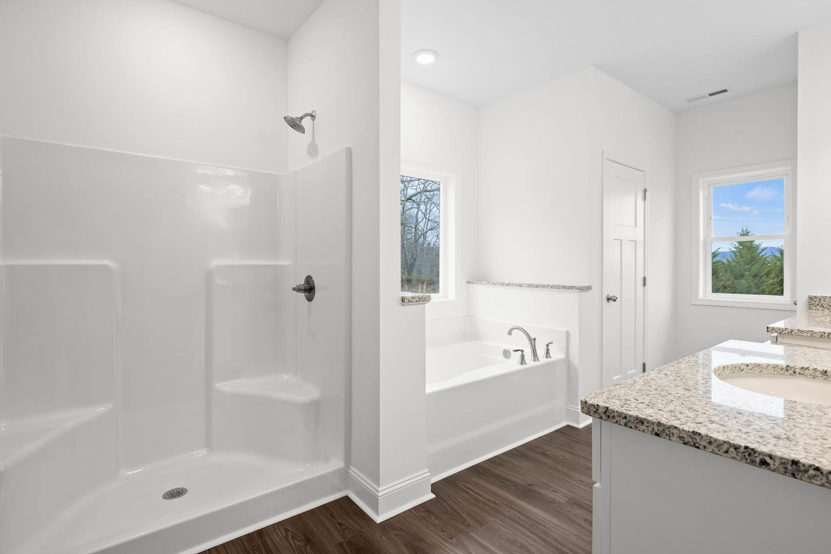 White tiled bathroom featuring a freestanding bathtub, glass-enclosed shower with chrome shower head, modern faucet, large window overlooking leafless trees, and minimalist