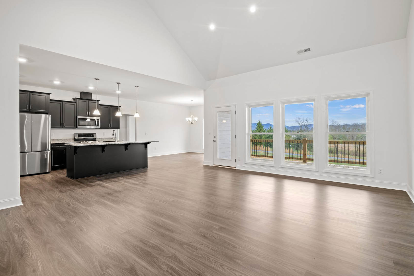 Spacious open floor plan featuring a kitchen island with black and white countertops, hardwood flooring, modern cabinetry, stainless steel refrigerator, and large windows