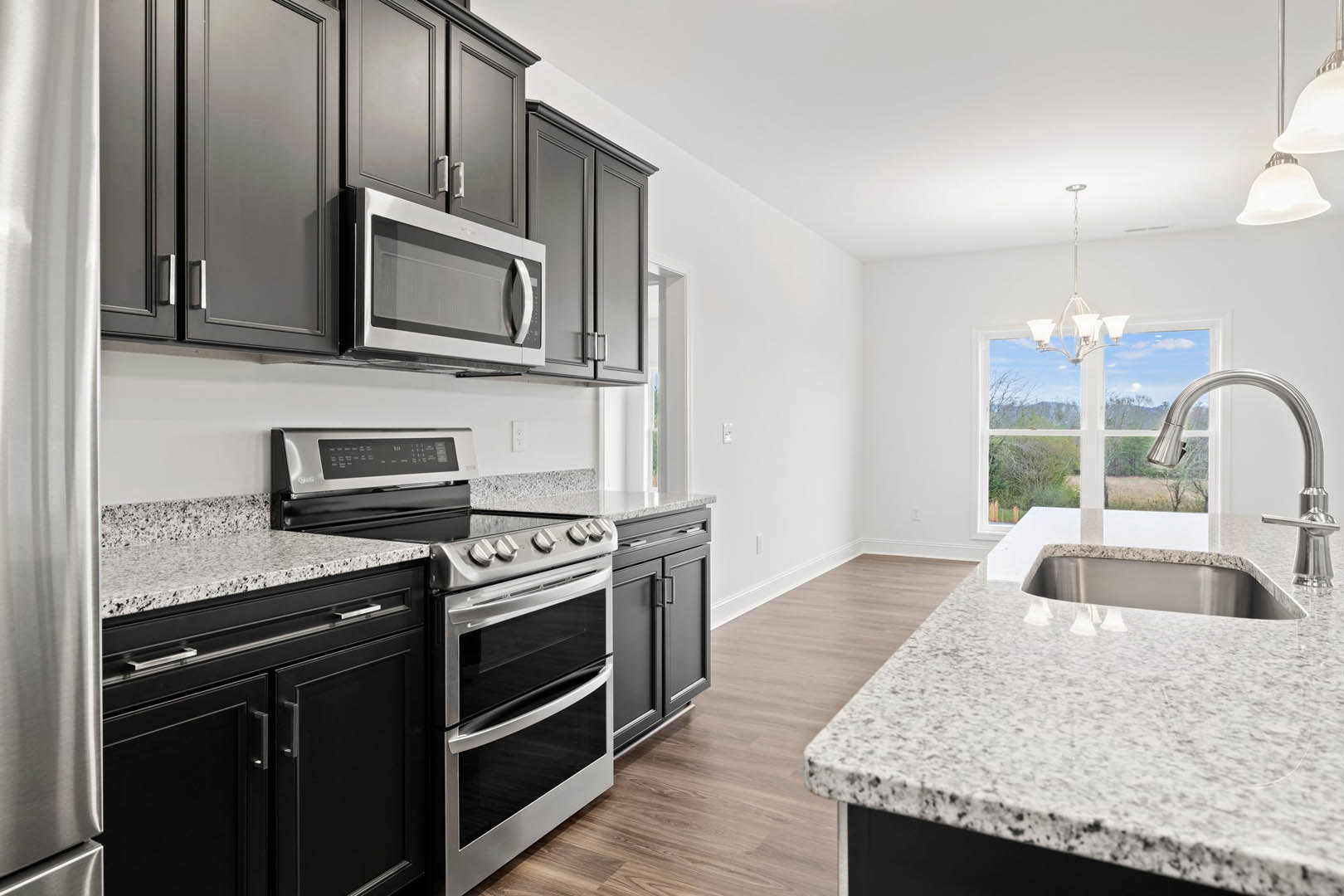 Black kitchen cabinets with polished granite countertops, stainless steel stove, glass-door microwave, undermount sink, and modern appliances