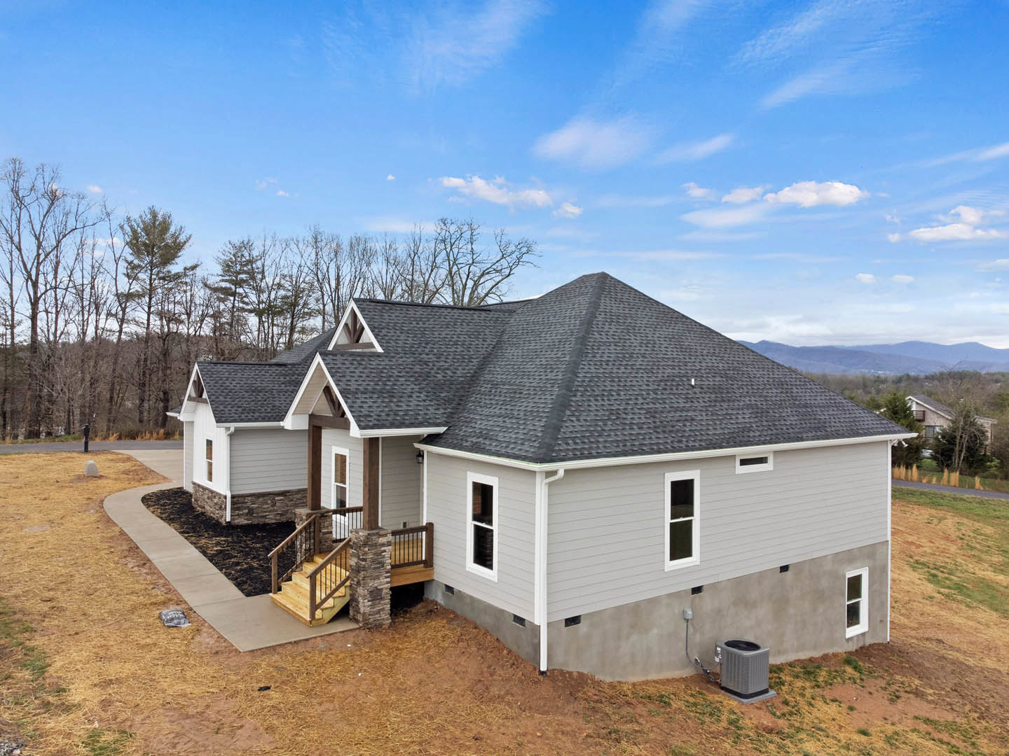 Two-story home with white siding, concrete driveway, wooden deck with stairs, white-framed windows, and gray roof surrounded by trees under a cloudy sky