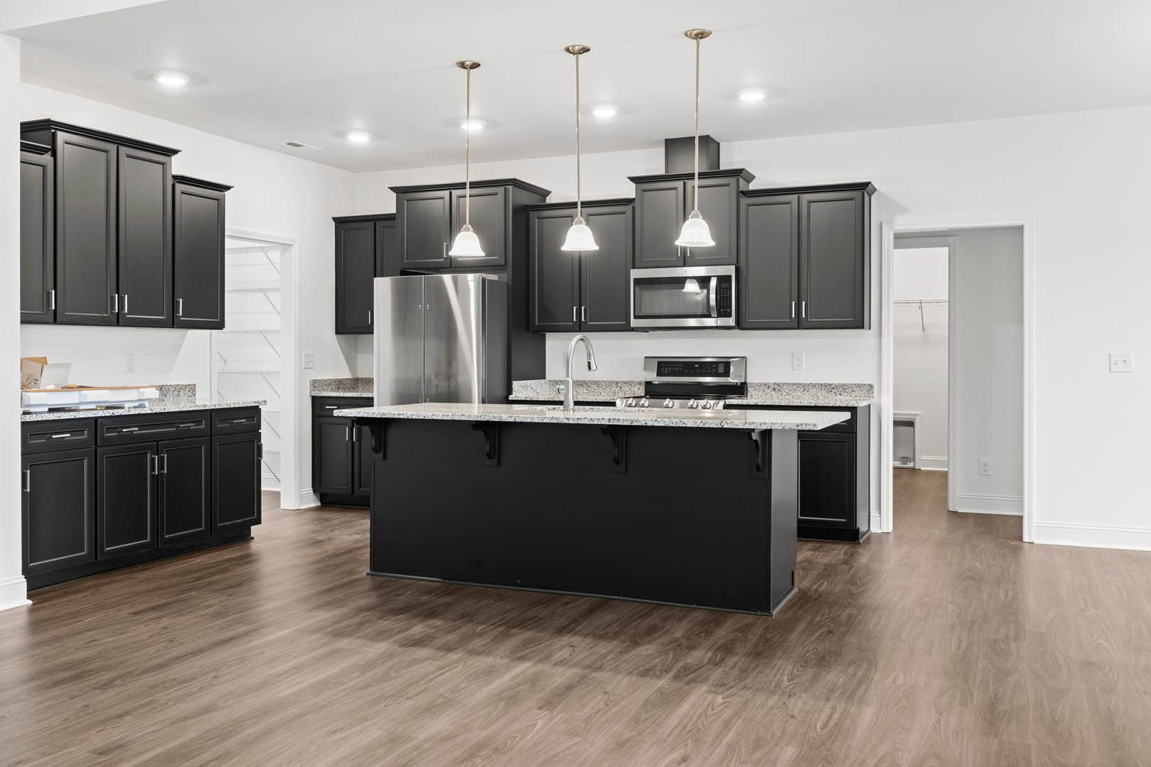 Black kitchen cabinets with stainless steel refrigerator, black and white countertops, built-in microwave, black and silver oven, and modern cabinetry