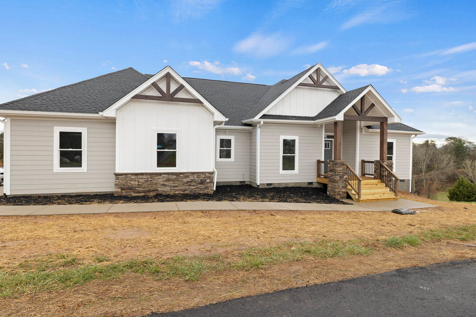 Two-story house with white-framed windows, covered front porch, wooden stairs with metal railings, and a driveway bordered by grass and dirt.