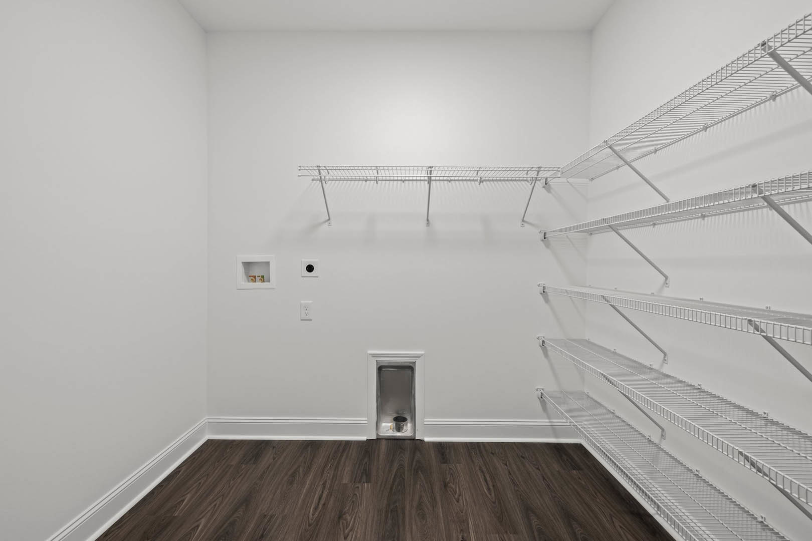 White empty room with dark wood flooring, white trim, and a small dog house; metal shelving and square white shelf with cutout visible against plaster walls.