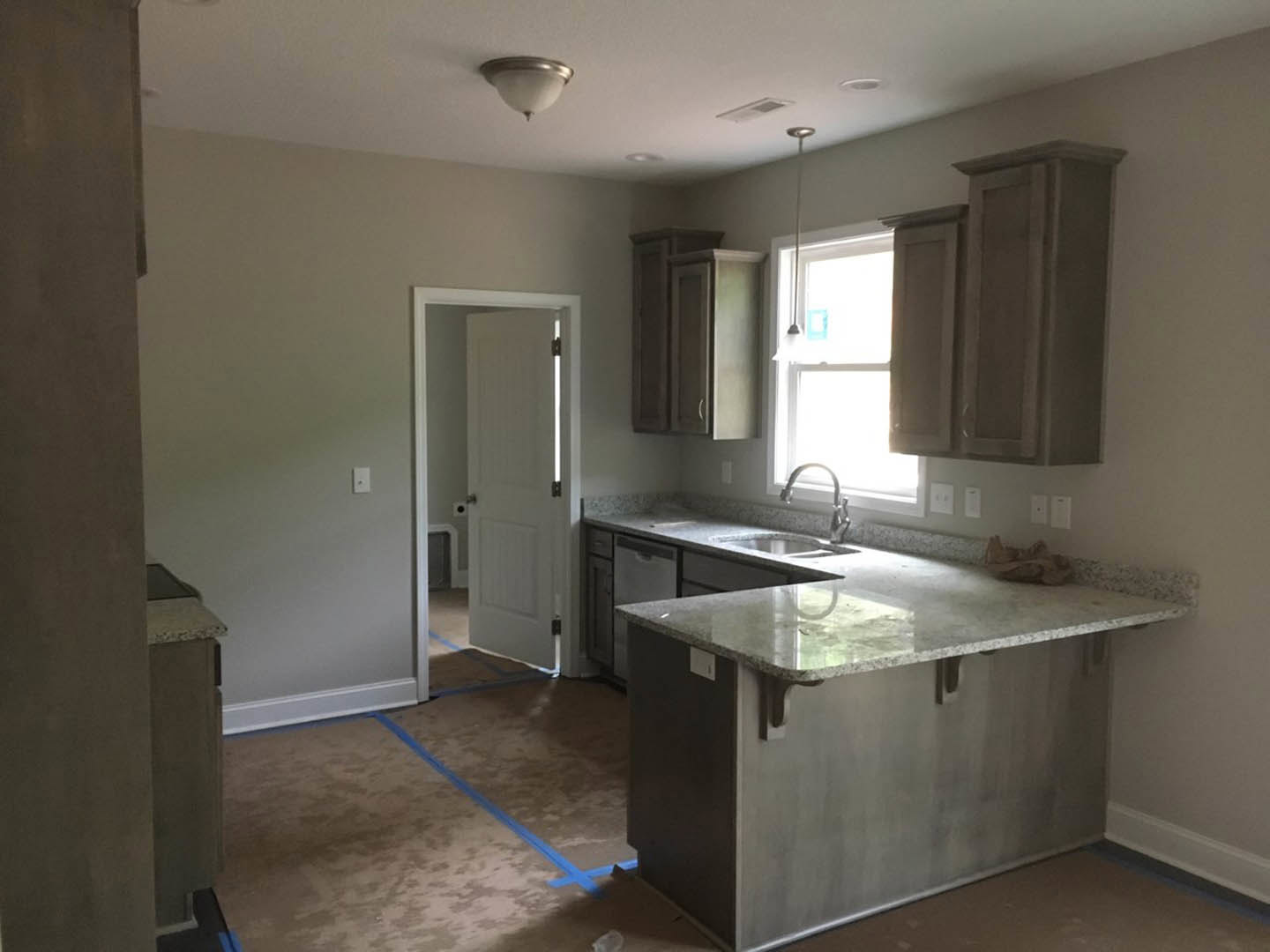 Modern kitchen featuring tile flooring, white cabinetry, stone countertop with stainless steel sink, window allowing natural light, white door, and blue painter’s tape on the floor