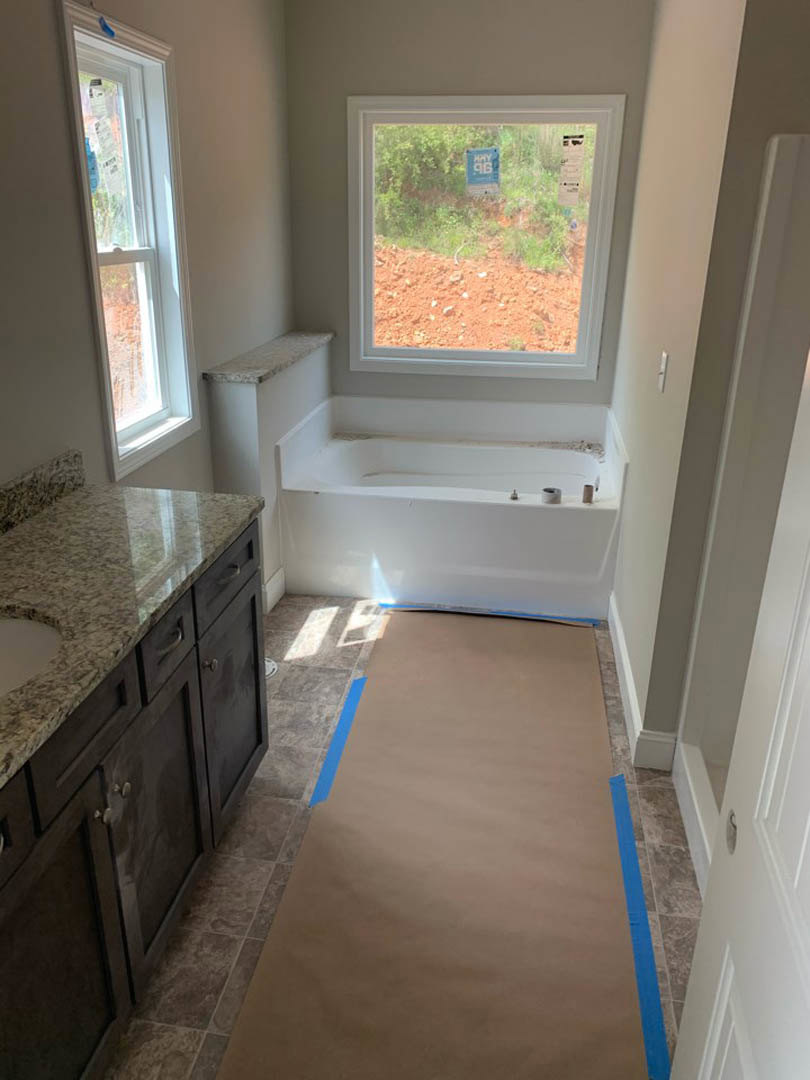 Bathroom with white-framed window, freestanding bathtub, marble countertop vanity, and tile flooring with brown paper covering