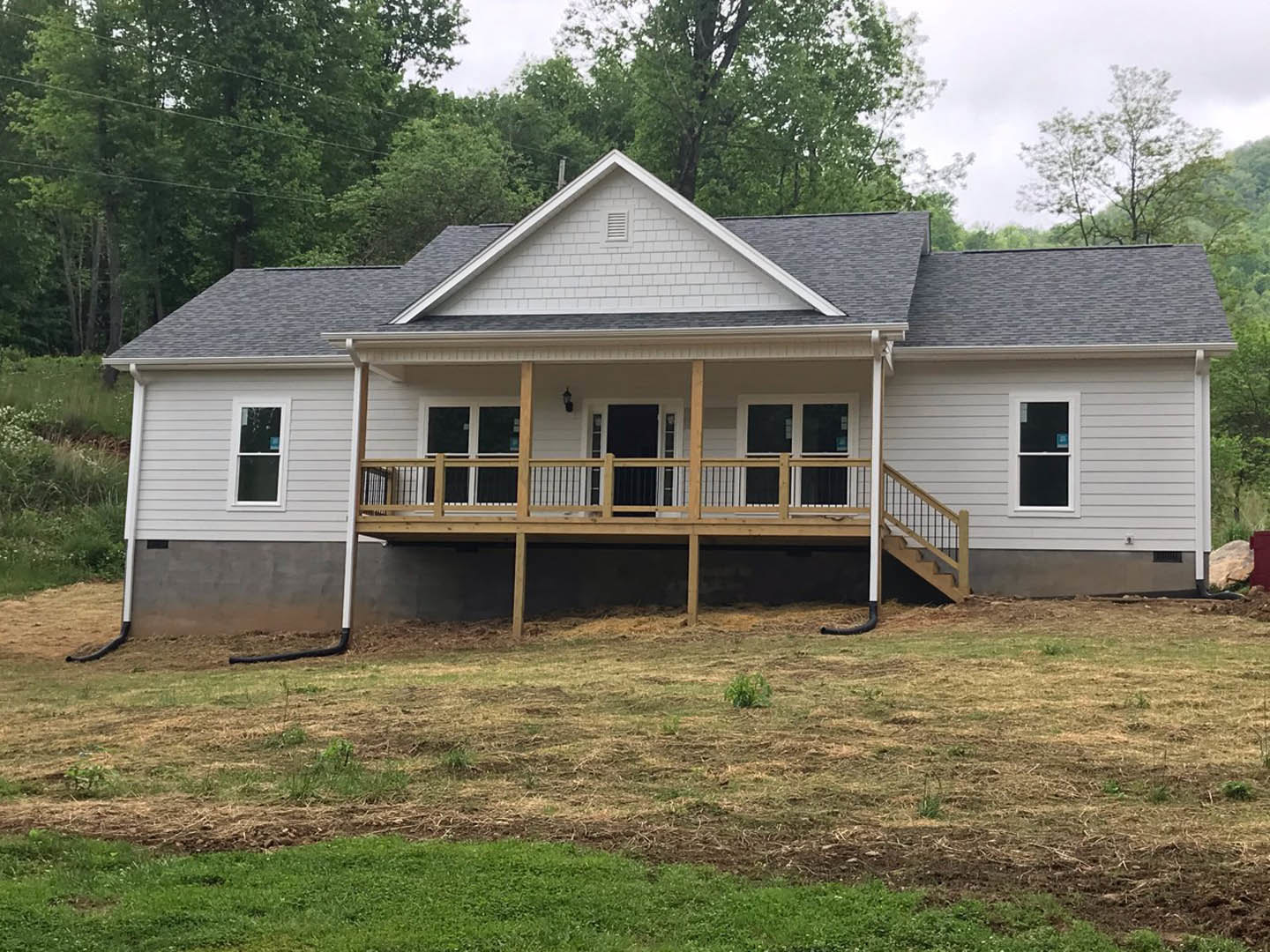 Two-story house with white siding, covered front porch with wooden railing, large windows with white frames, manicured lawn bordered by a wooden fence, mature trees in the