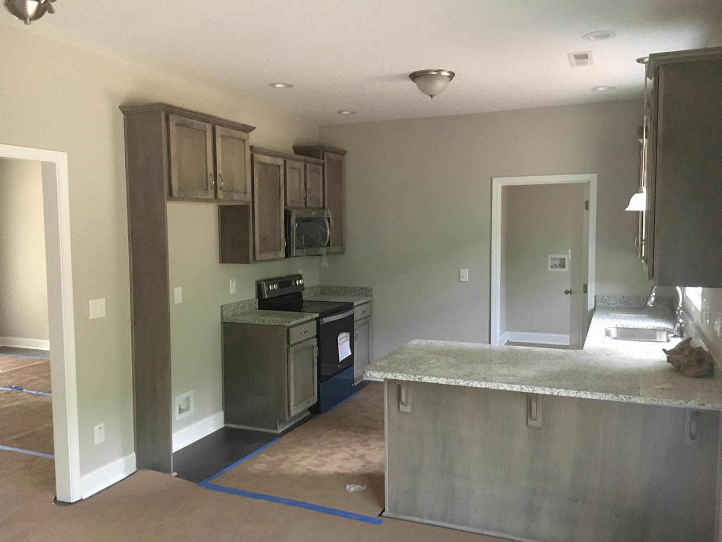 Modern kitchen featuring light stone countertop with undermount sink, white tile backsplash, built-in shelving on white wall, stainless steel microwave, recessed lighting, and