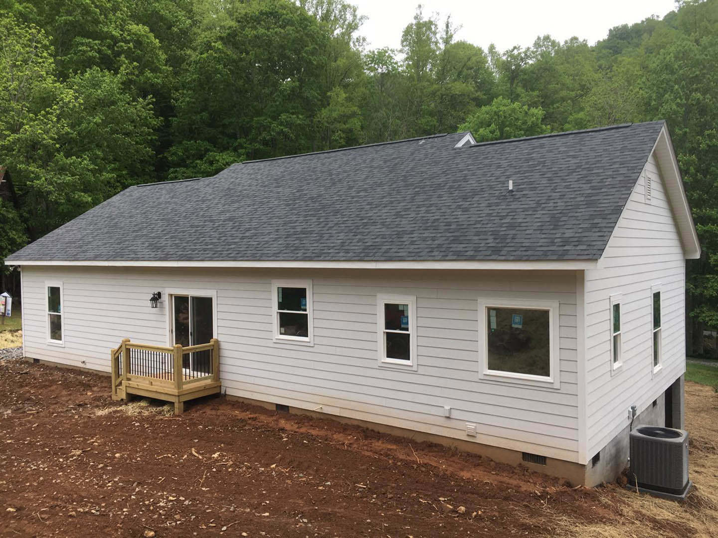 White siding house with covered porch, wood deck featuring metal railing, white-framed windows, and a grey storage bin with black lid on the deck.