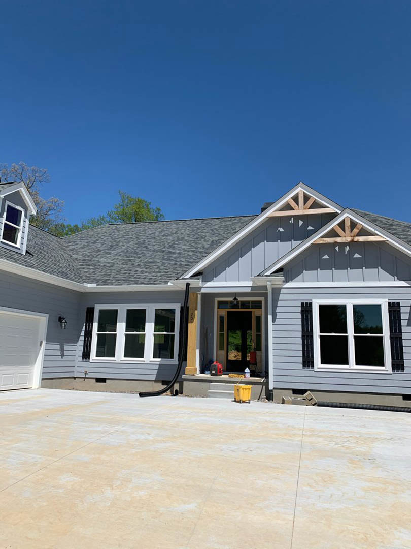 Two-story house with light siding, attached garage, paved driveway, and large windows under a clear blue sky