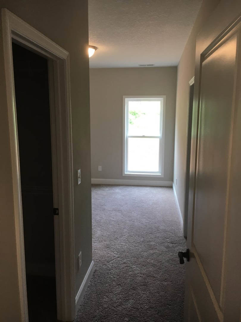 Hallway with carpeted walls, white-framed window, open door, and neutral flooring