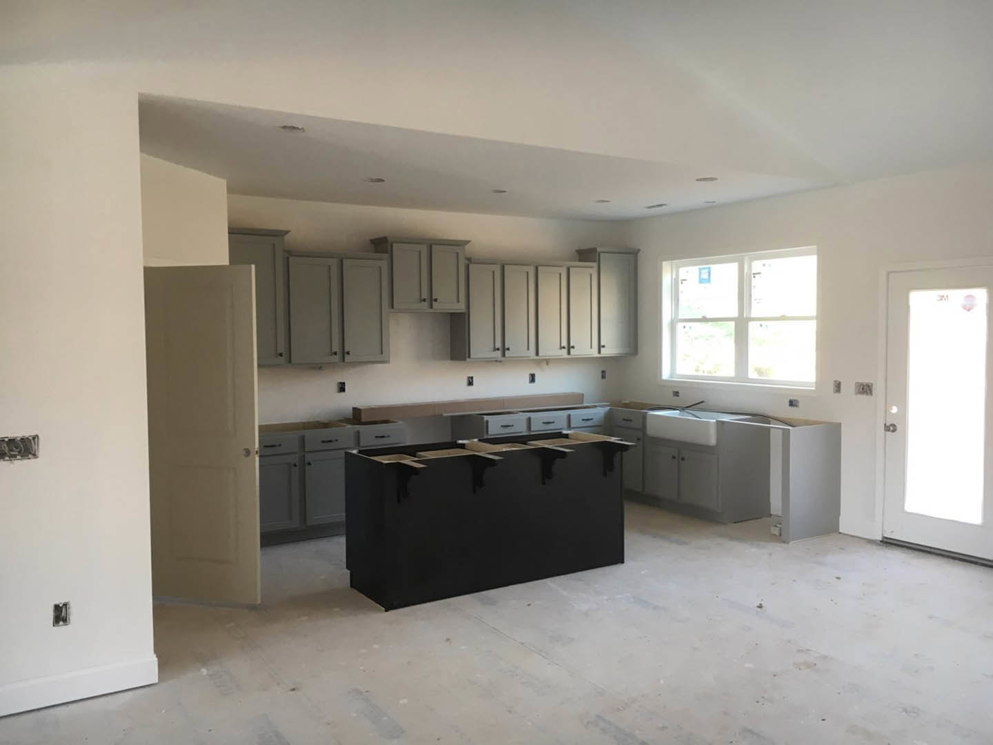 Modern kitchen featuring black countertops, white cabinetry with silver handles, tile flooring, a window with a white frame, and a white door illuminated by natural light.