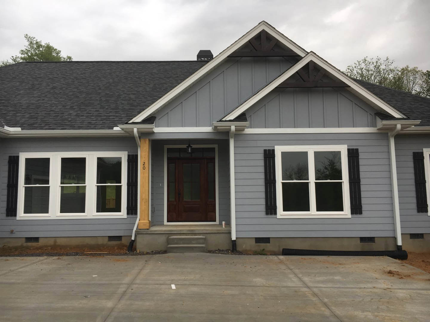 Two-story home with grey roof, white siding, black-trimmed windows, concrete driveway, and dark front door under covered entry.