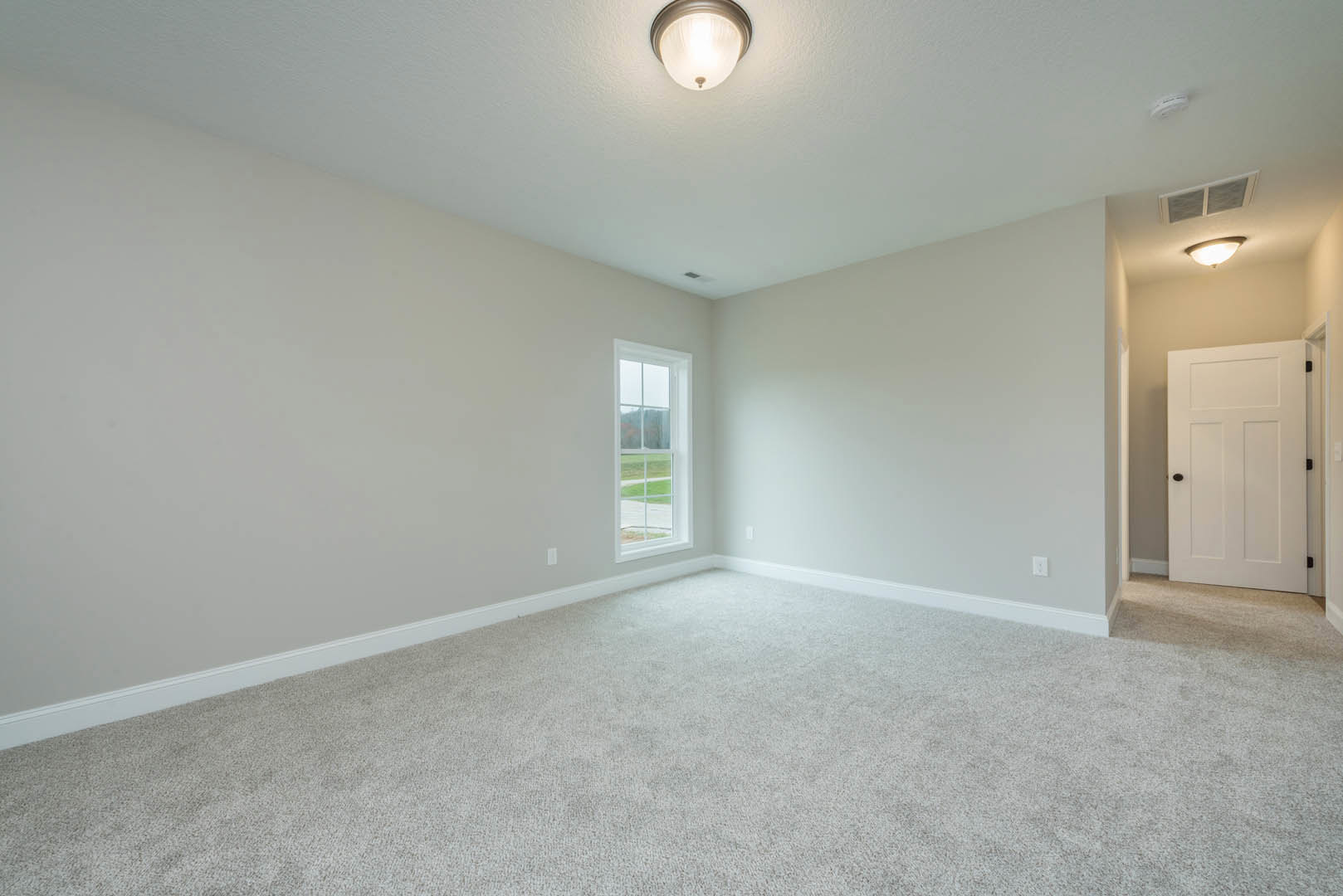 Carpeted room with a ceiling light fixture, white door with black handles, window overlooking a grassy field, white walls, and crown molding