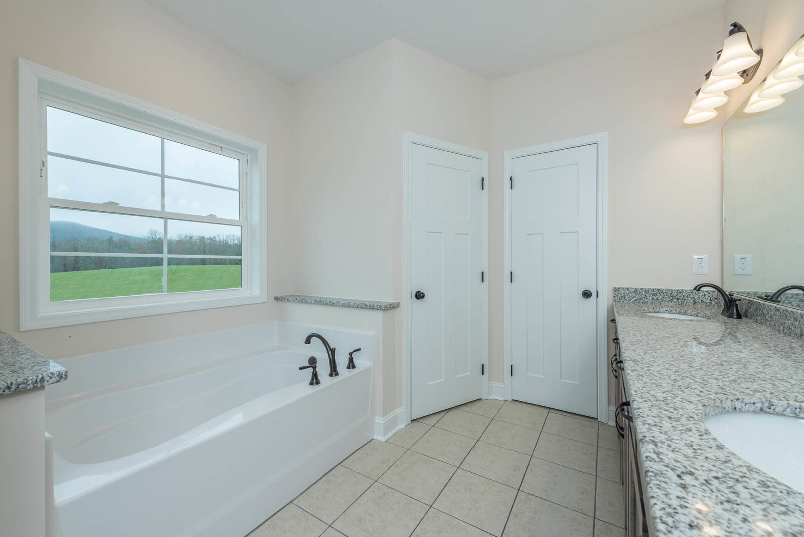Bathroom featuring a freestanding bathtub with chrome faucet, marble countertop sink, white paneled door with black hardware, large window overlooking a field and trees, light tile